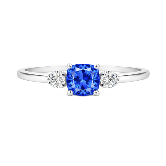Blue sapphire engagement ring with 6 mm cushion center and 3 mm round side stones, crafted in white gold-plated 925 silver. Available now at BSI Jewelry.