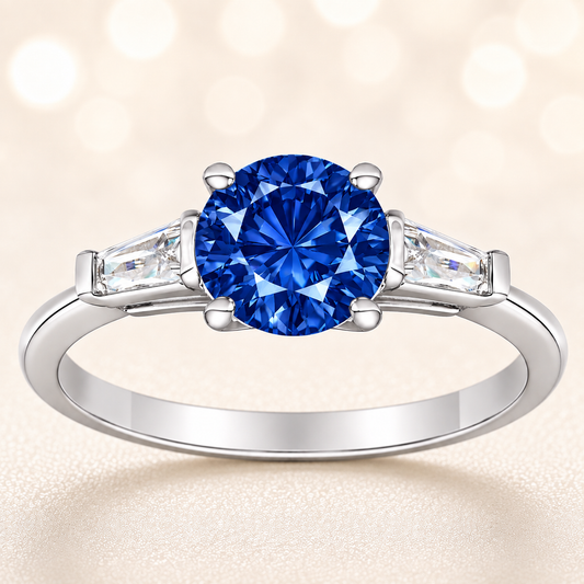 Blue sapphire ring, 6 mm round, with tapered moissanite accents in white gold-plated 925 silver. Elegant and timeless. Available now at BSI Jewelry.