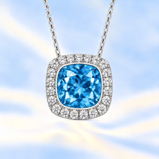 Swiss blue topaz cushion pendant, 6 mm cushion center with halo, crafted in white gold-plated 925 silver. Fresh, bright, and elegant. Available now at BSI Jewelry.