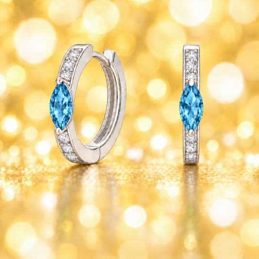 Huggie earrings with Swiss blue topaz marquise and Moissanite accents in white gold-plated 925 silver. Hypoallergenic, safe to wear. Available at BSI Jewelry.