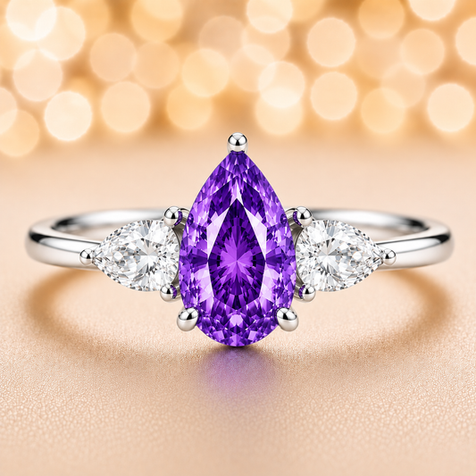 Purple sapphire ring with 7×5 mm pear center and side stones in white gold-plated 925 silver. Elegant and refined for daily wear. Available now at BSI Jewelry.