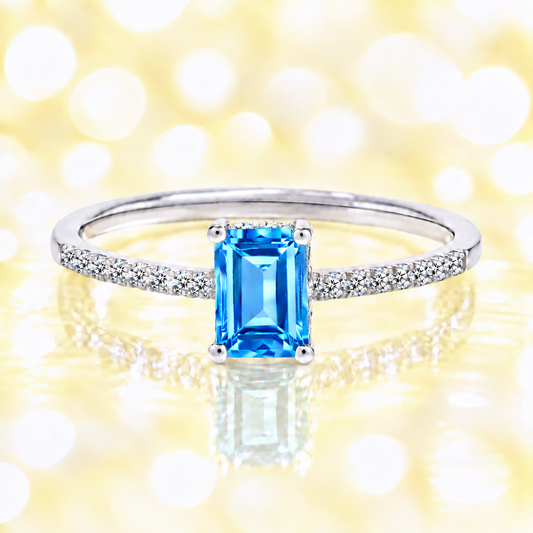 Swiss blue topaz ring with a 7×5 mm emerald cut in white gold-plated 925 silver, with moissanite. Elegant and refined for daily wear. Available now at BSI Jewelry.